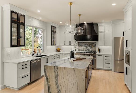 A luxury kitchen remodel featuring white modern drawers and cabinets with a marble island and glass ball hanging lights