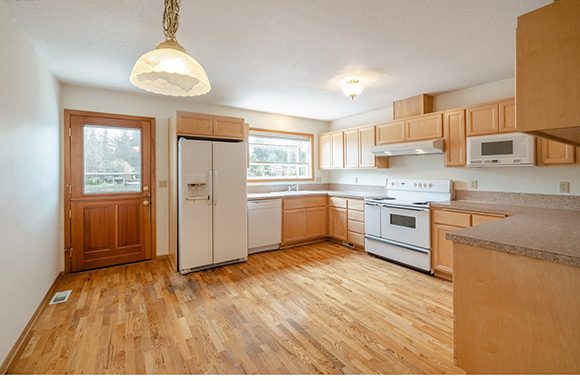 An outdated kitchen with worn out hardwood floors and generic cabinets and white kitchen accessories