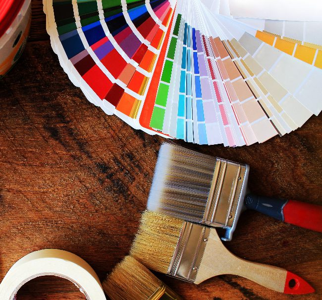 Paint brushes and color swatches on a wood table to help illustrate how to choose paint colors.