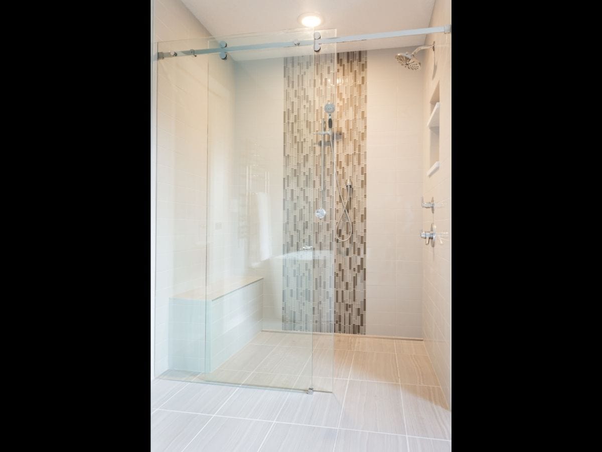 A luxury shower with clear sliding glass door and custom light brown tile
