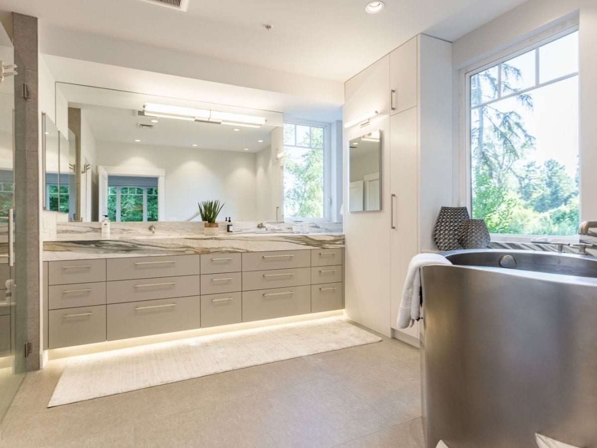 A luxury bathroom remodel featuring light gray drawers with stainless steel accessories and toe kick lighting